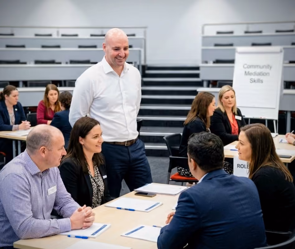 Thomas Gaultier standing over a table of participants working through a role-play during a community mediation skills workshop